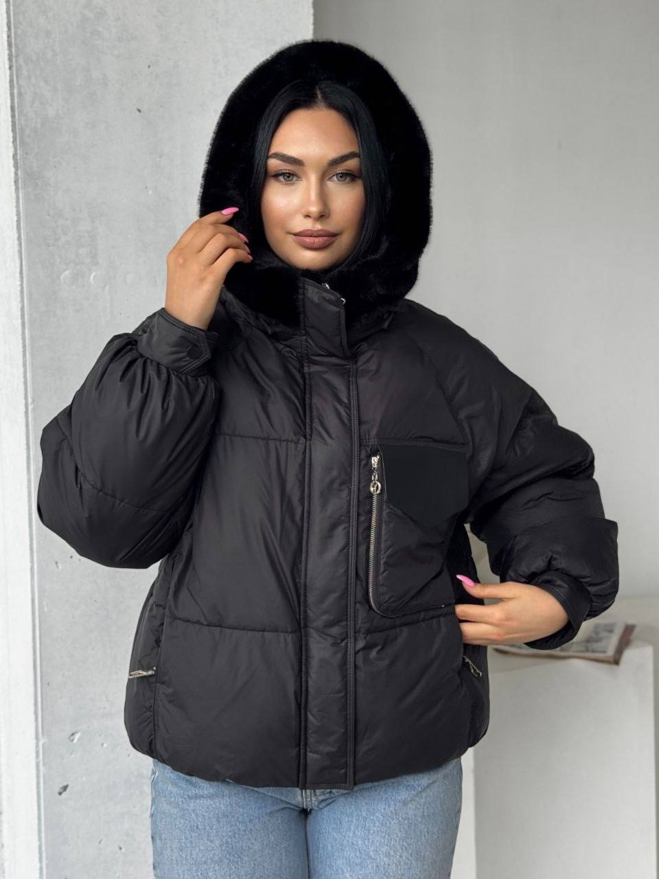 Woman wearing a black puffer jacket with fur hood against a neutral background