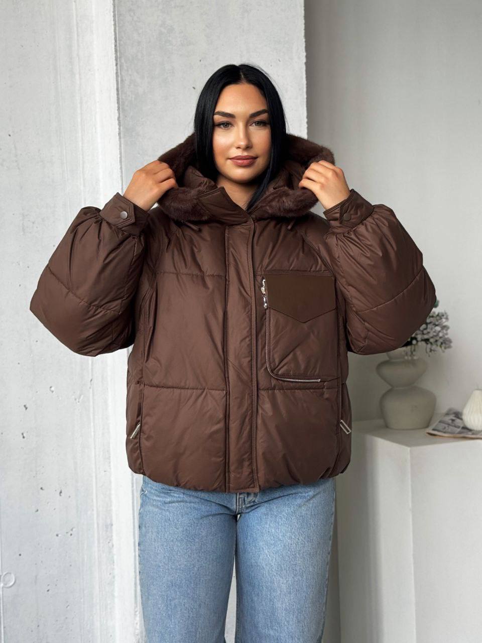 Person wearing a brown puffer jacket indoors against a light-colored wall.