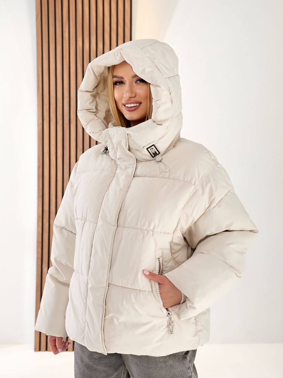 Person wearing a beige puffer jacket with a hood against a white background