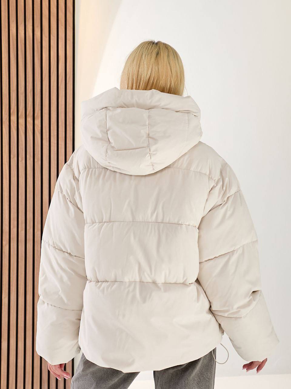 Person wearing a beige puffer jacket with a plain background