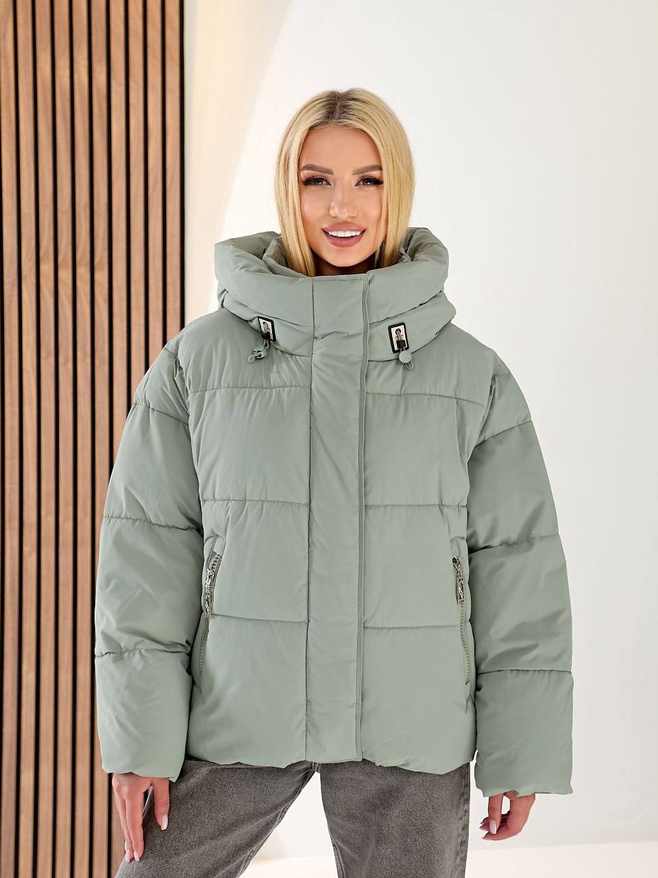 Person wearing a green puffer jacket with a neutral background