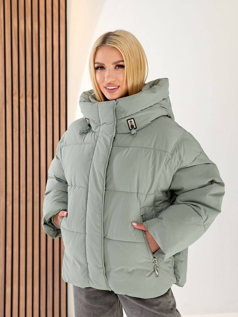 Woman wearing a light green puffer jacket against a neutral background