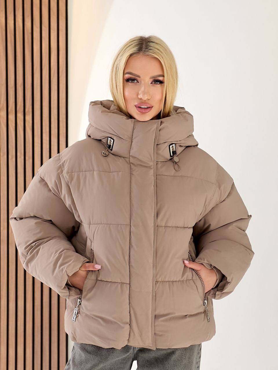 Woman wearing a beige puffer jacket against a white background