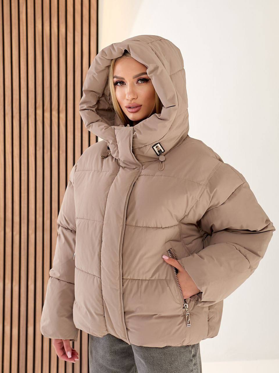 Woman wearing a beige puffer jacket with a hood against a neutral background