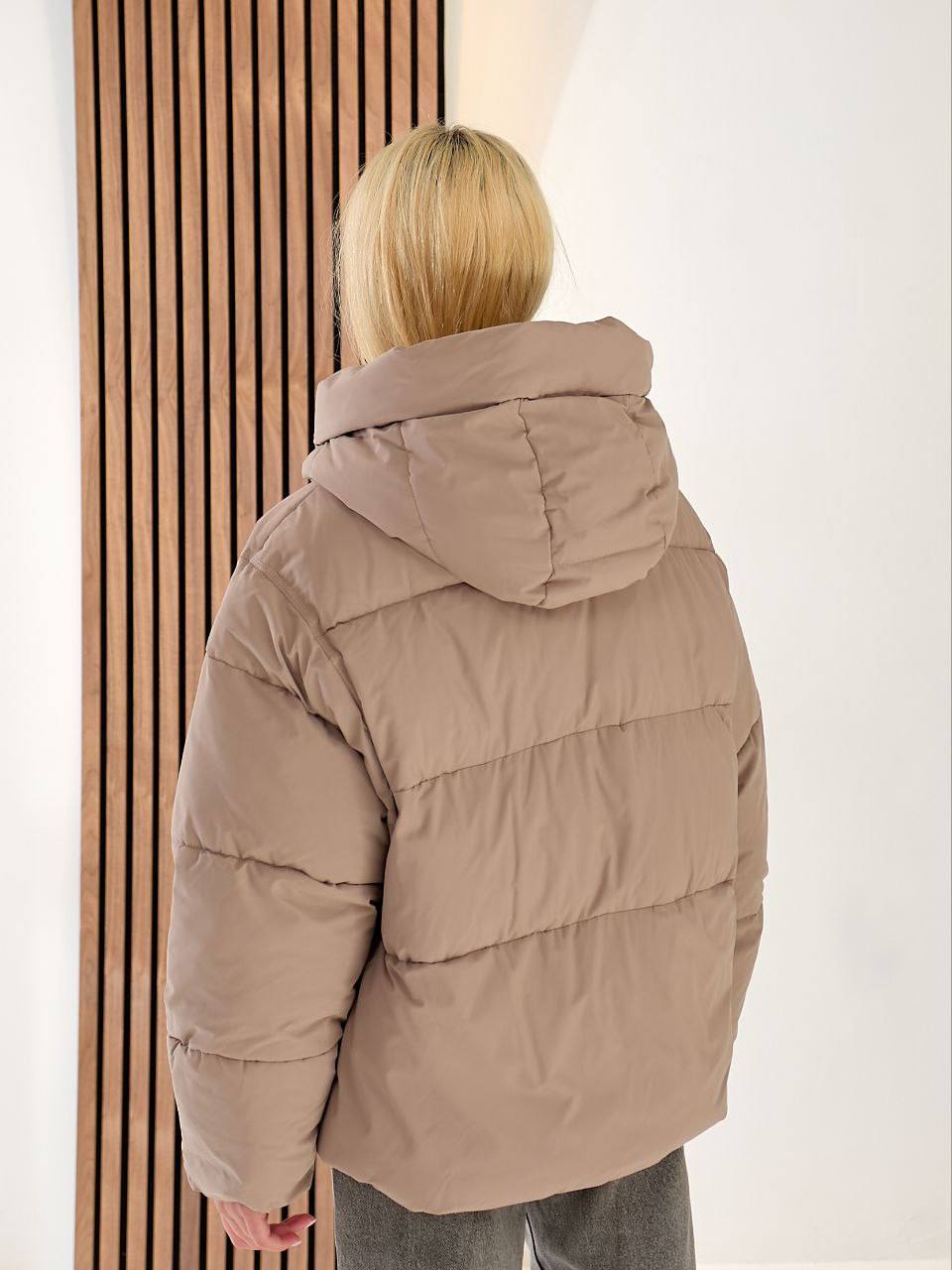 Person wearing a beige puffer jacket standing against a light-colored wall.