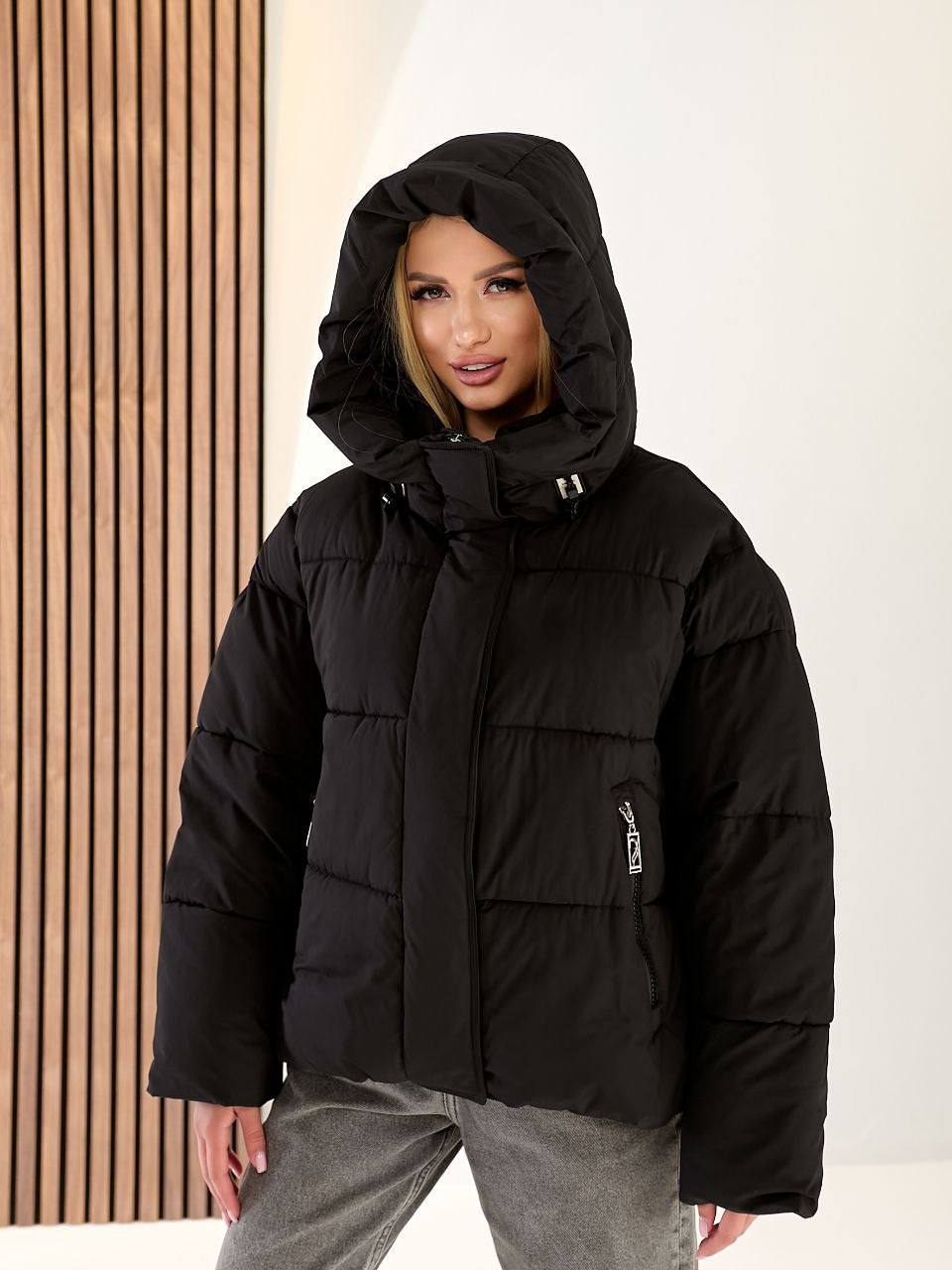 Person wearing a black puffer jacket with a hood against a neutral background