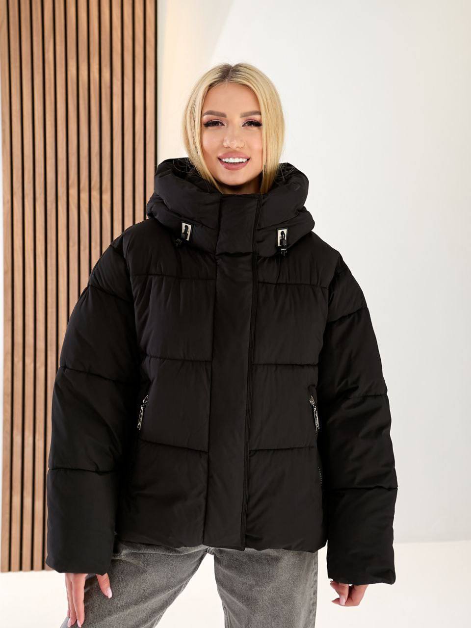 Person wearing a black puffer jacket standing against a neutral background