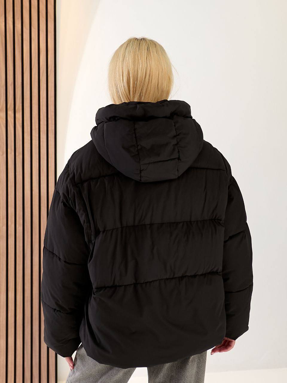 Person wearing a black puffer jacket with a hood against a neutral background
