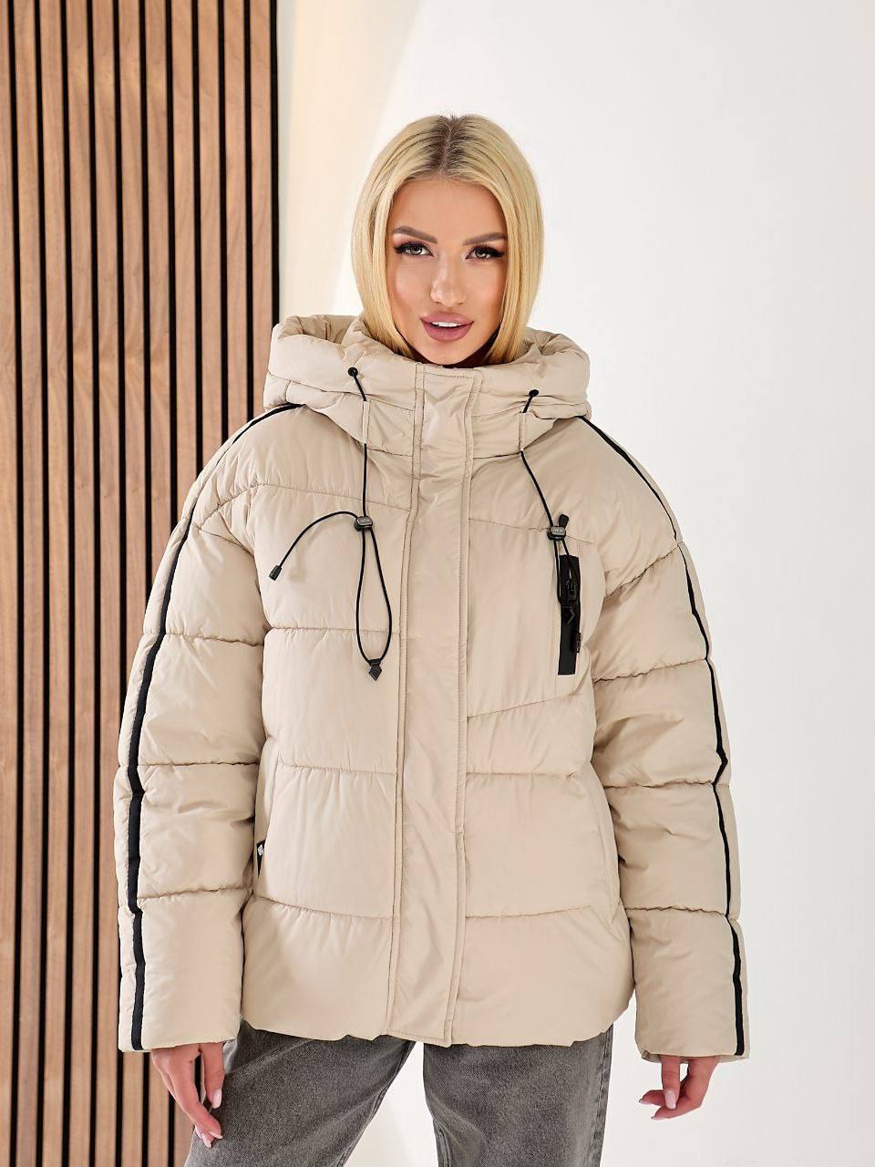 Woman wearing a beige puffer jacket with black accents against a neutral background