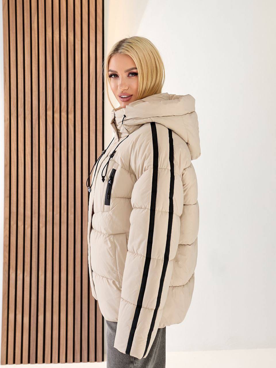Woman wearing a beige puffer jacket with black stripes indoors.