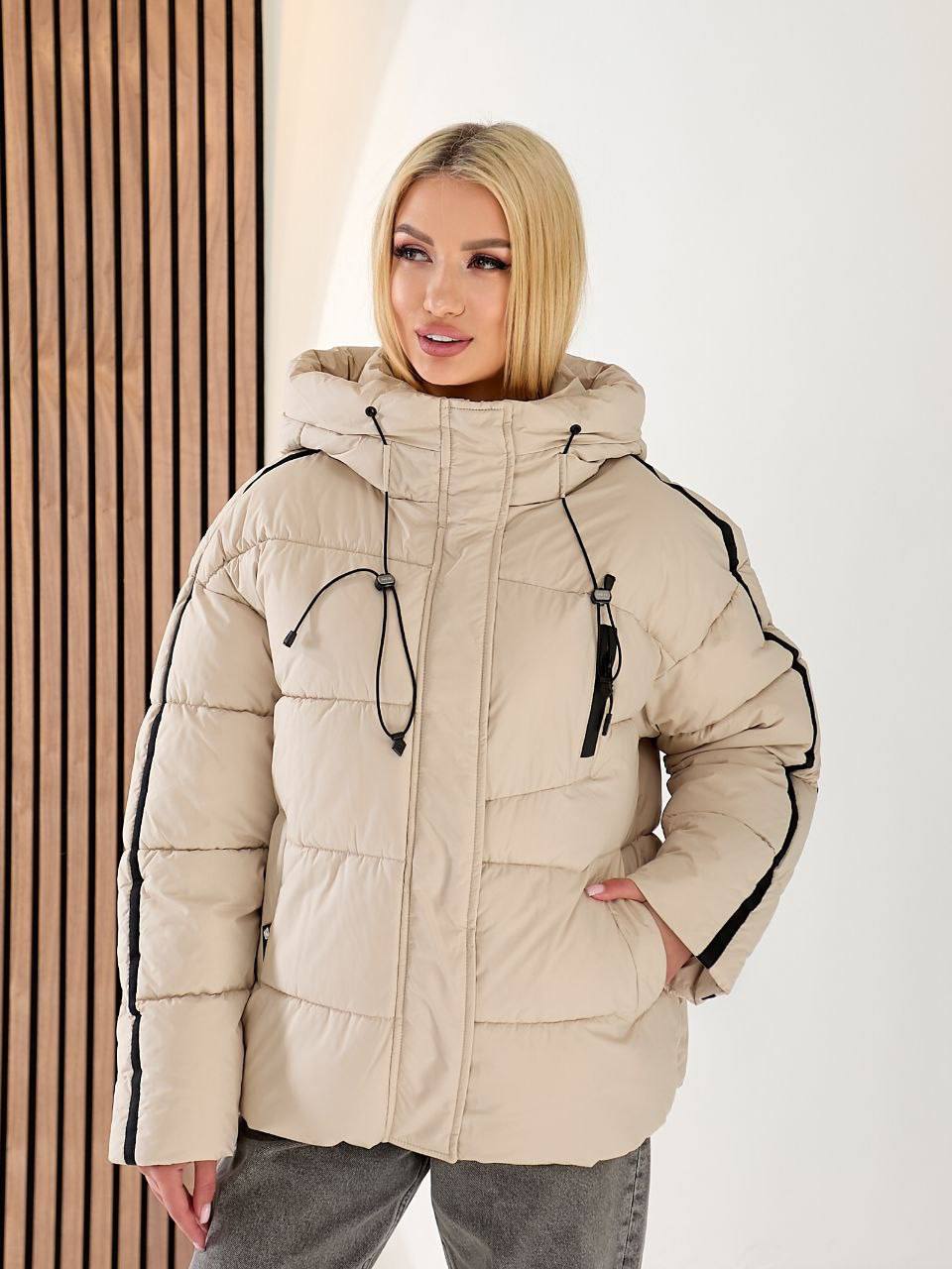 Woman wearing a beige puffer jacket with black accents against a white background