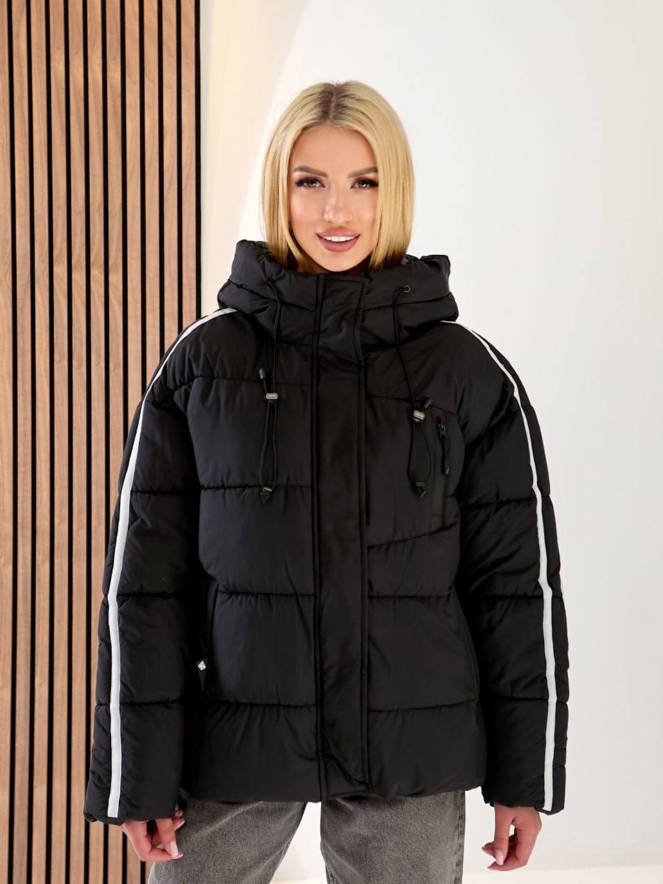 Woman wearing a black puffer jacket with white stripes on a plain background