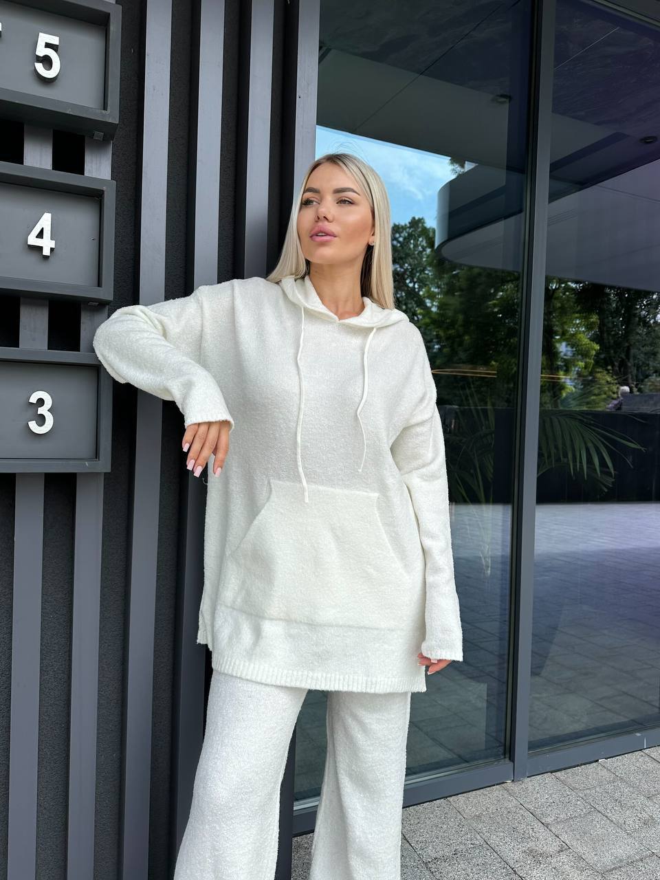 Woman in a white outfit standing in front of a modern building entrance.
