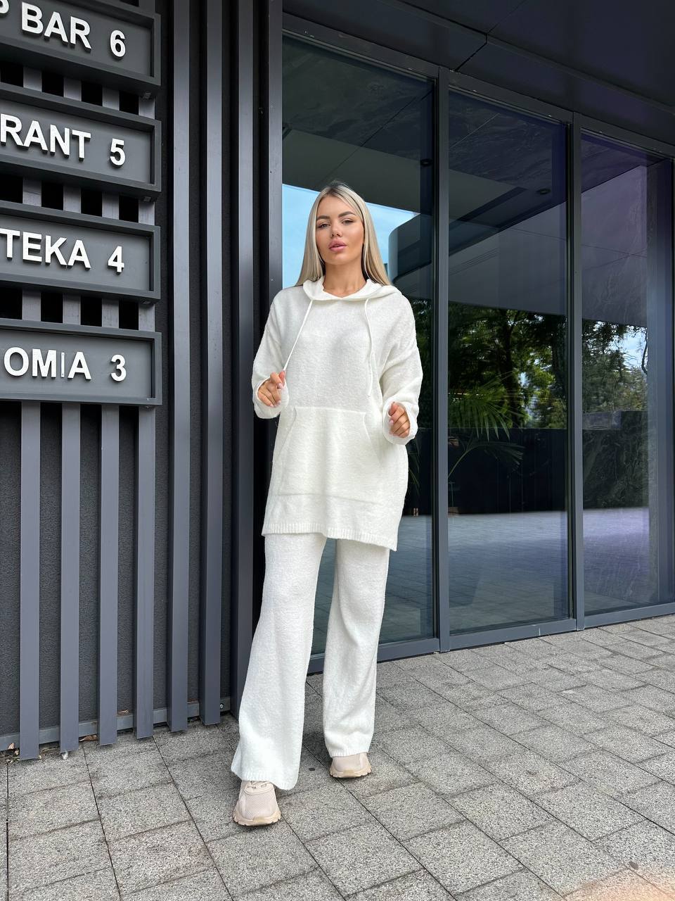 Woman in a white outfit standing outside a modern building with glass doors.