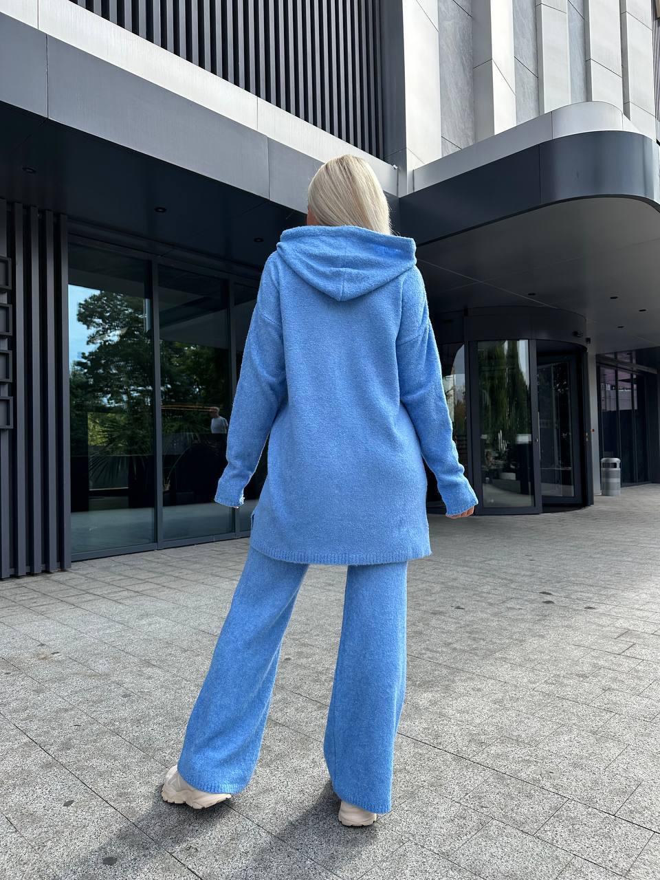 Person wearing a blue outfit walking outside a modern building.