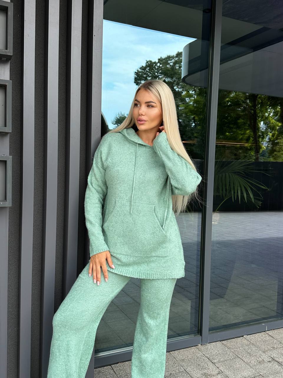 Woman in a mint green tracksuit standing outside a building with glass doors.