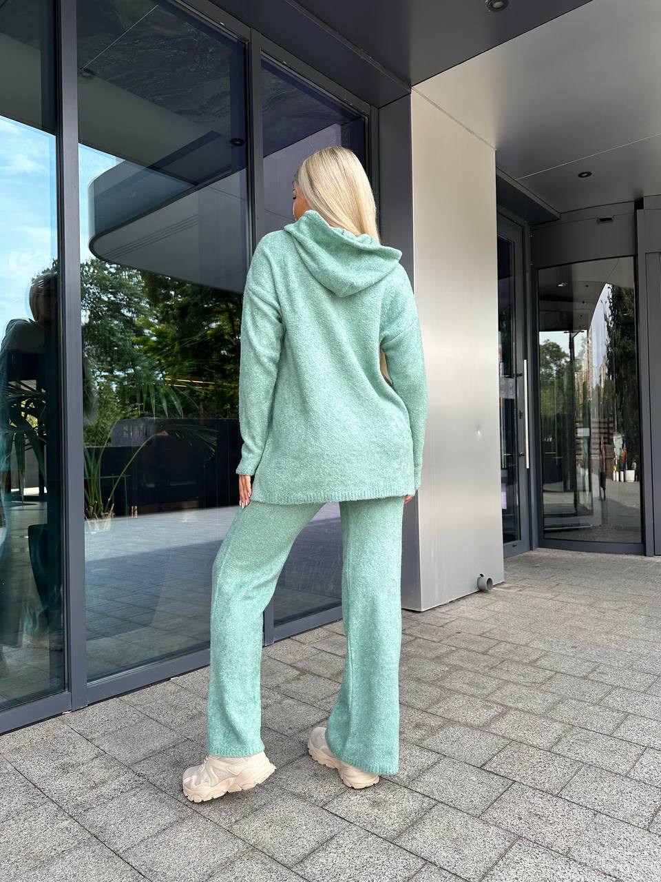 Person wearing a light green tracksuit standing outside a modern building.