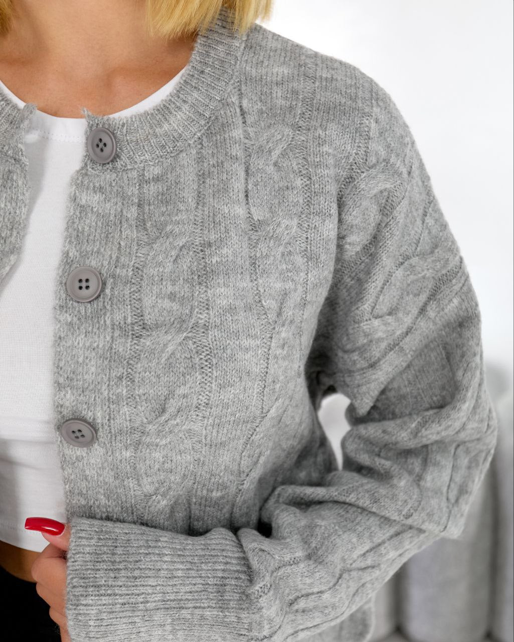 Gray cable knit cardigan worn over a white shirt with a blurred background