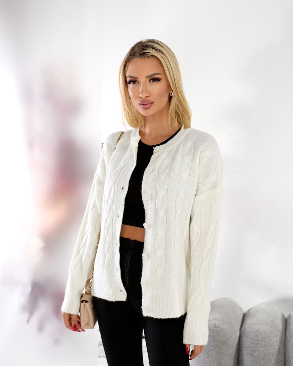 Woman wearing a white jacket over a black top and pants on a blurred background