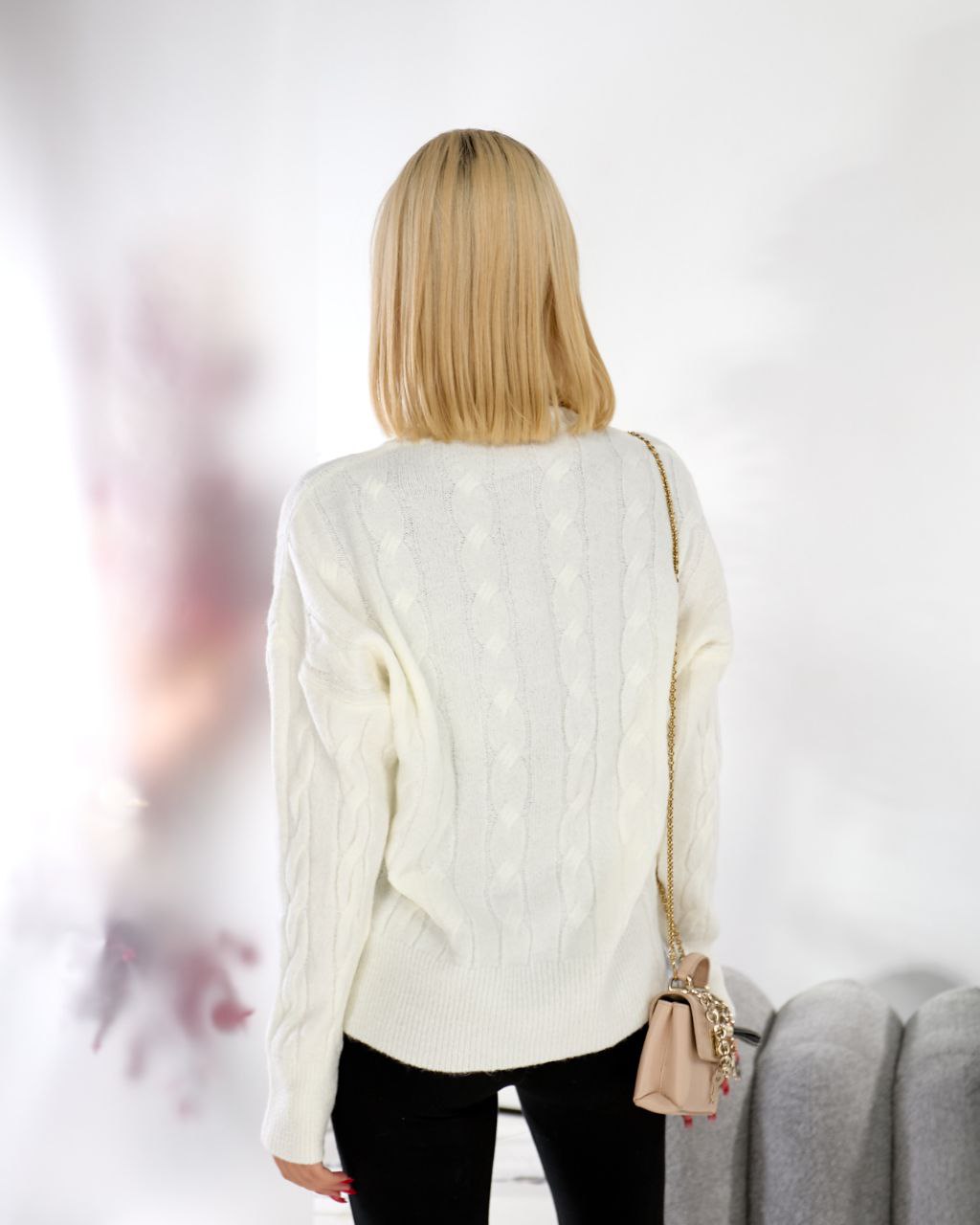 Person wearing a white cable knit sweater with a blurred background