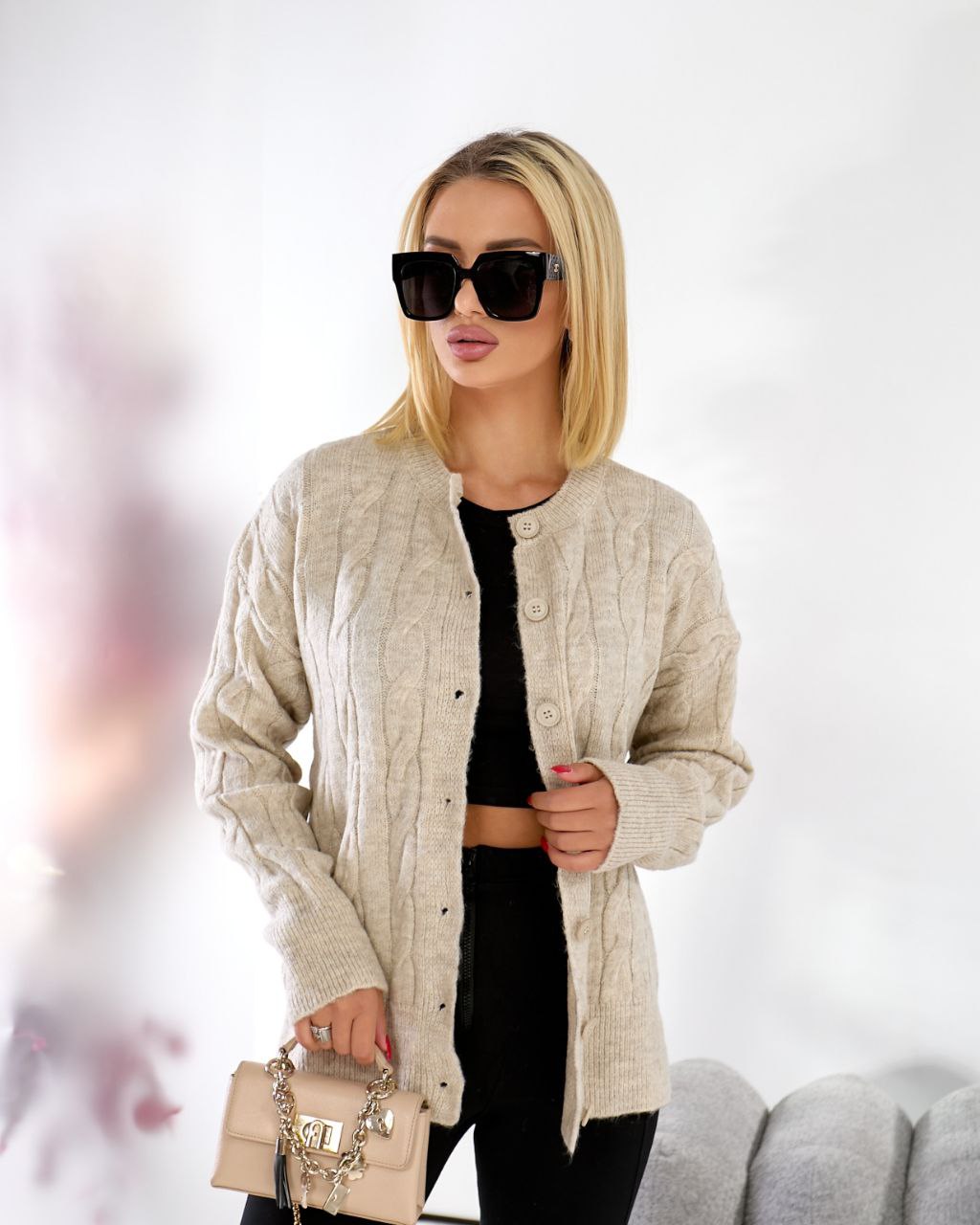 Woman wearing a beige cardigan and sunglasses with a blurred background