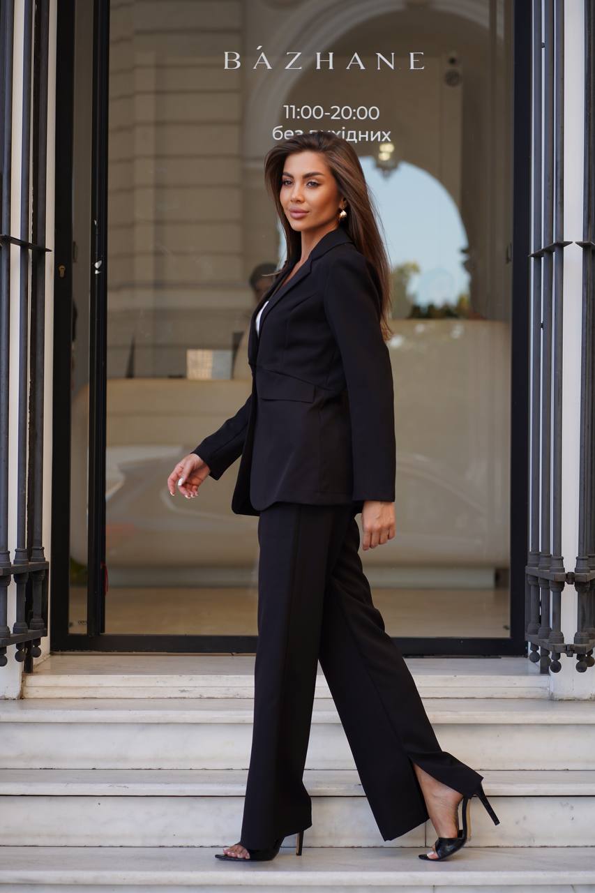 Woman in a black suit standing in front of a store entrance with 'Bázhane' branding.