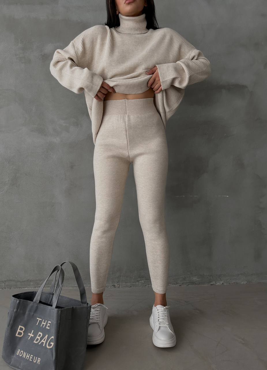 Person wearing a beige knit sweater and pants with a gray bag labeled 'B+Bag' on a gray background