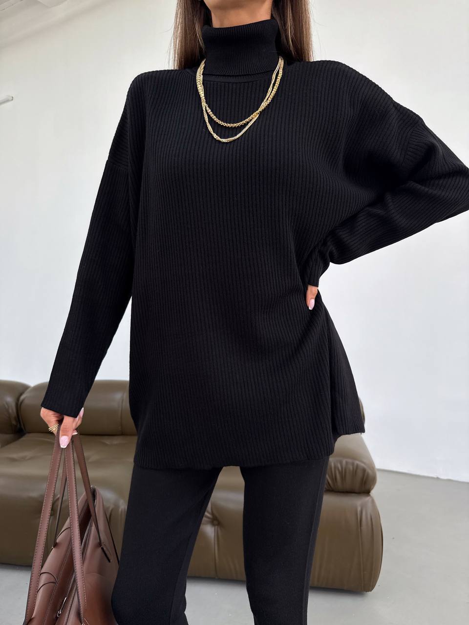 Person wearing a black sweater and pants holding a brown bag against a neutral background