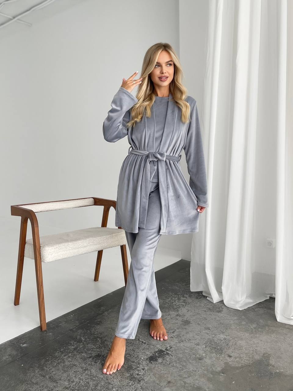 Woman wearing a gray robe in a room with a chair and curtains.