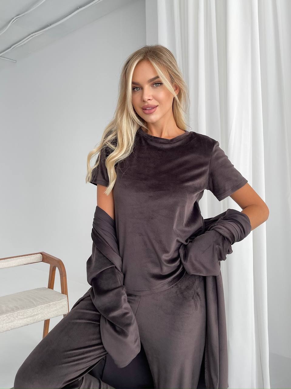 Woman wearing a dark brown outfit in a minimalistic room.