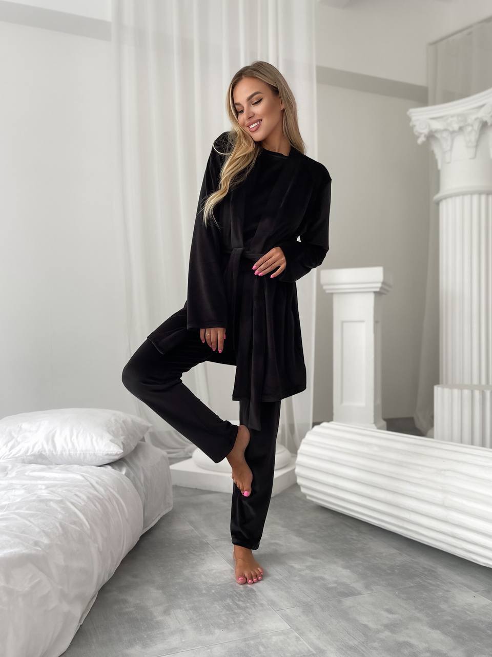 Woman in a black robe standing in a bedroom with white bedding and decor.