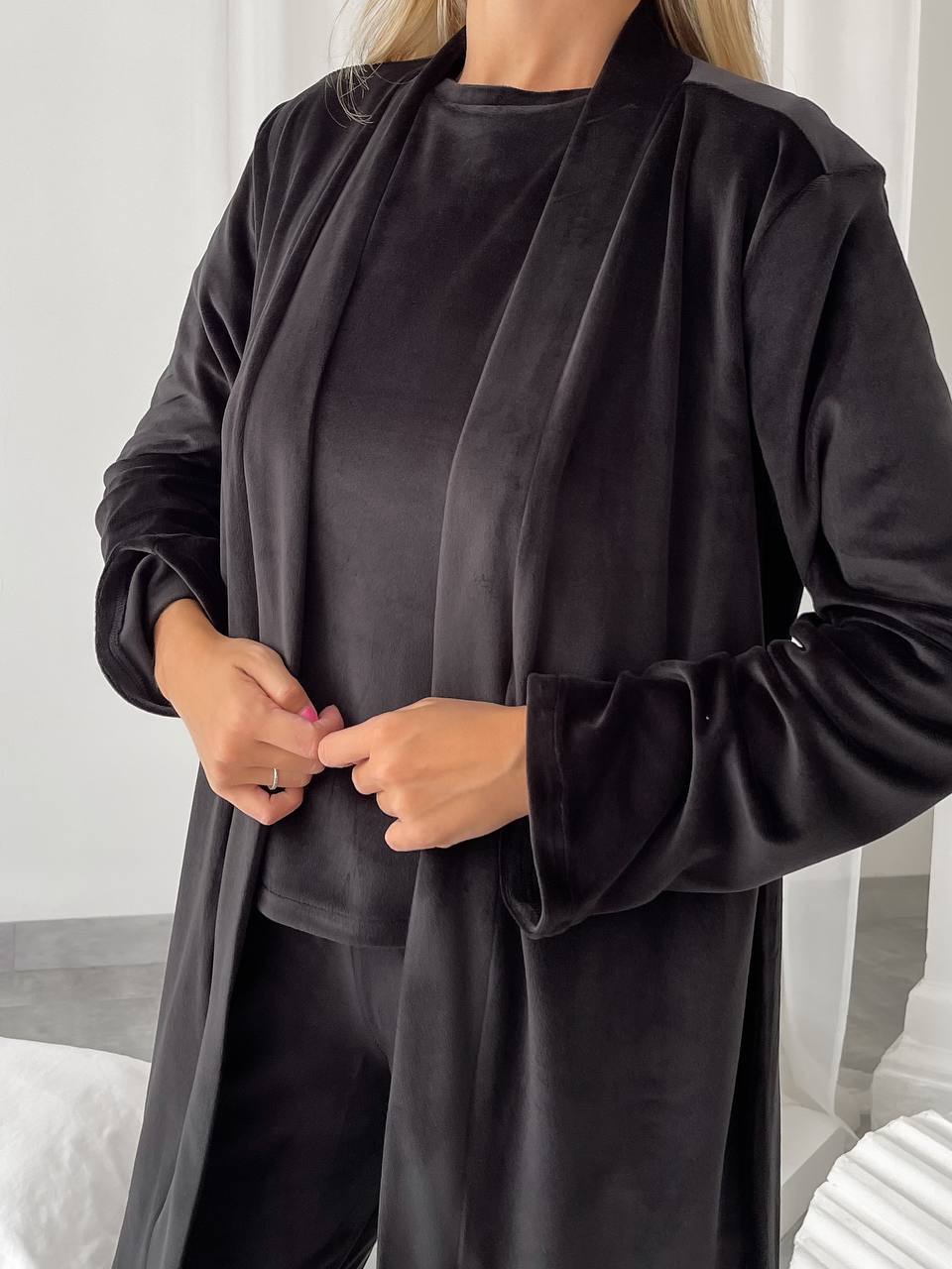 Person wearing a black long-sleeve shirt and pants with a matching coat indoors.