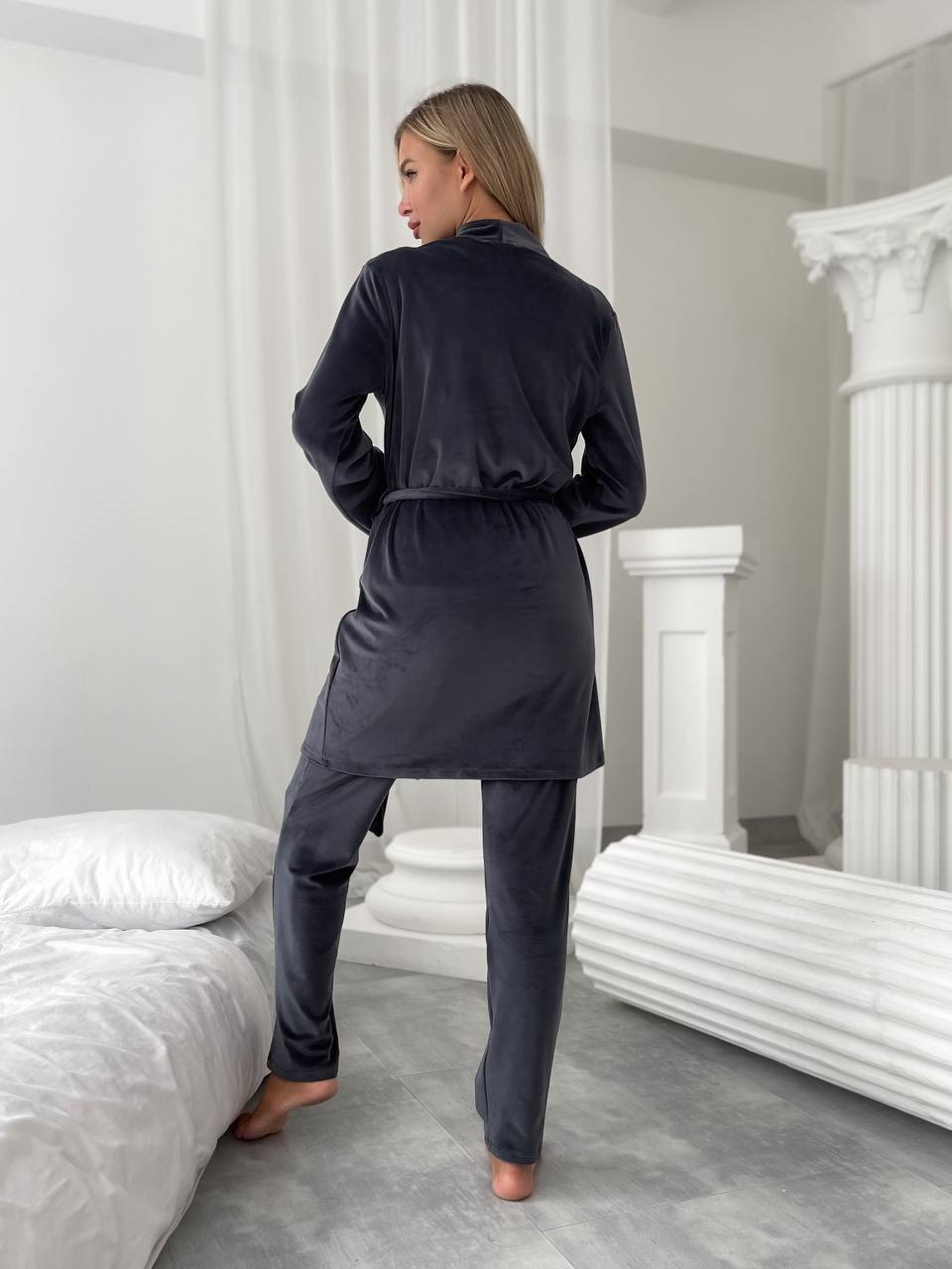 Woman wearing a dark gray pajama set in a bedroom.