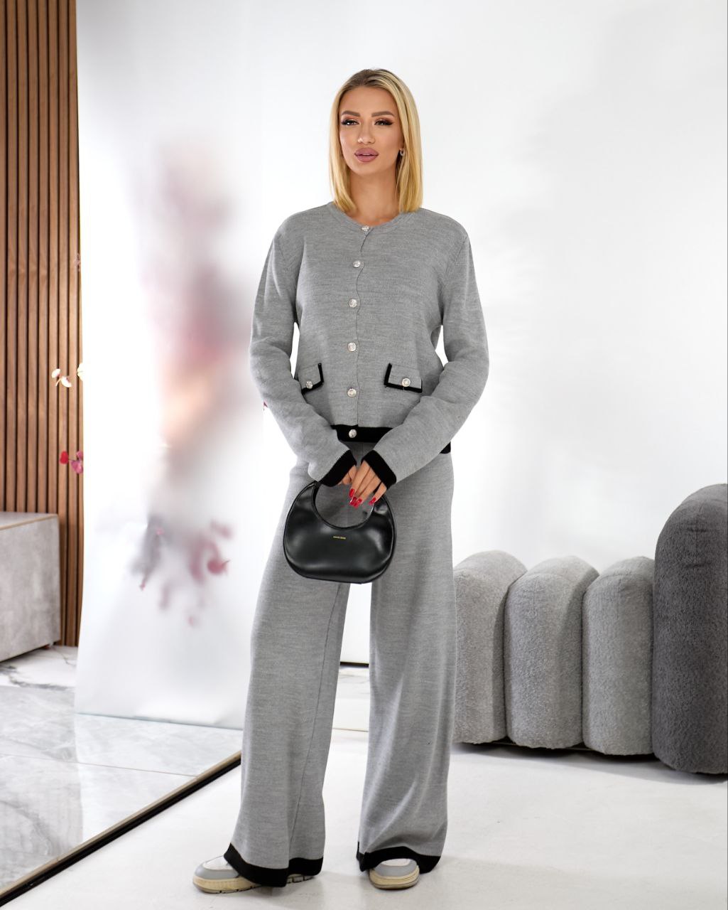 Woman wearing a gray outfit with a black handbag in an indoor setting