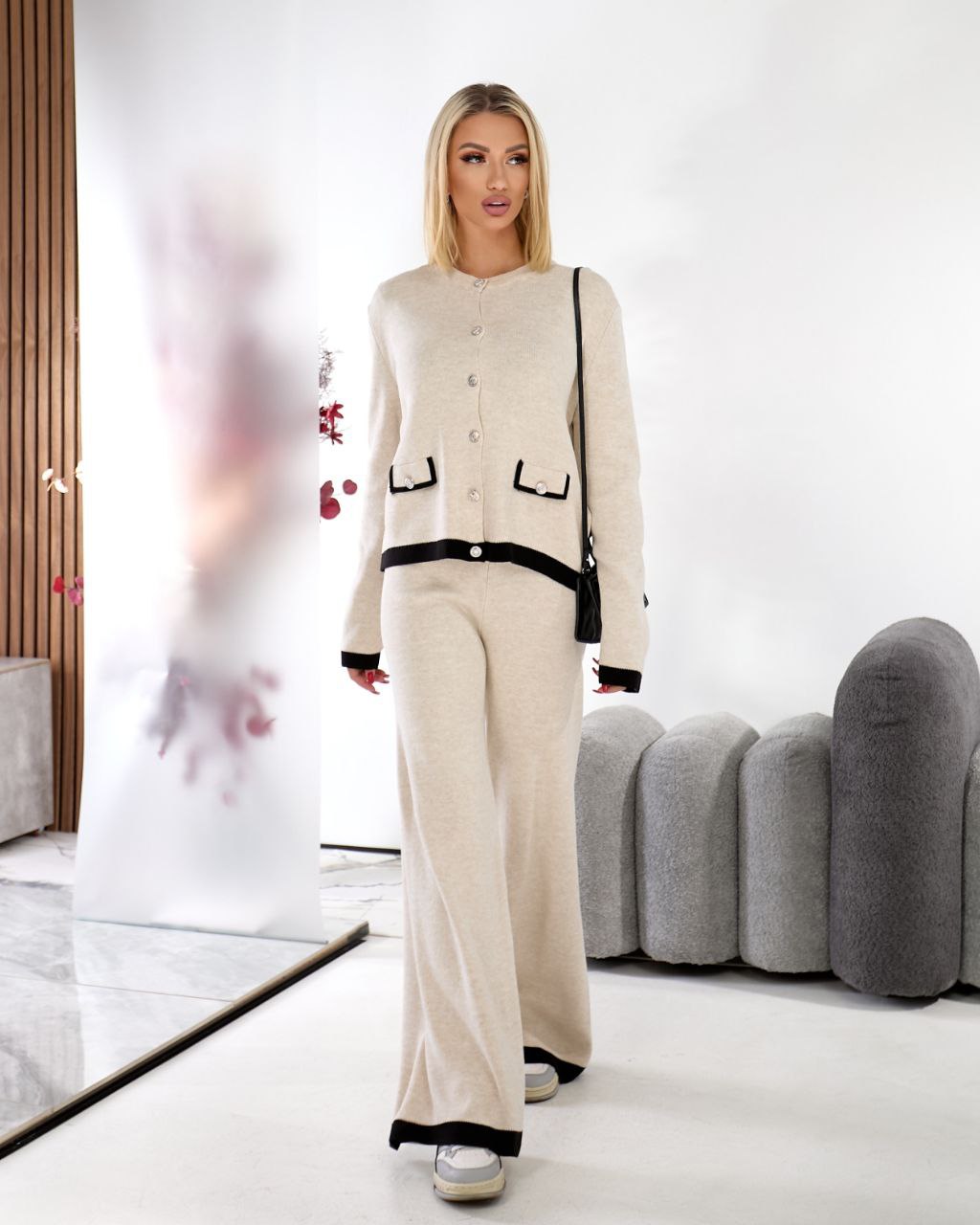 Woman wearing a beige outfit with black accents in a modern room.