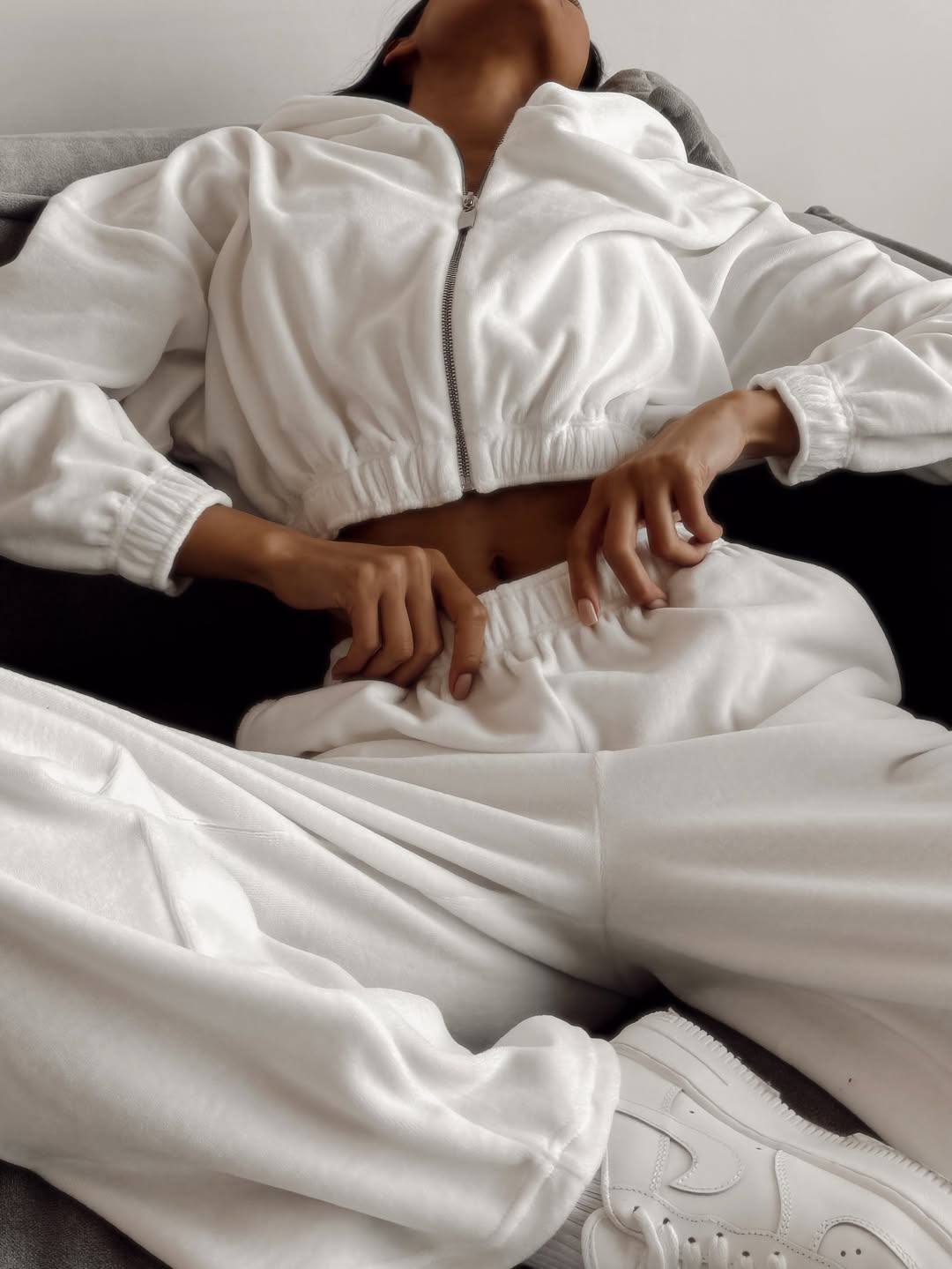 Person wearing a white tracksuit sitting on a bed.