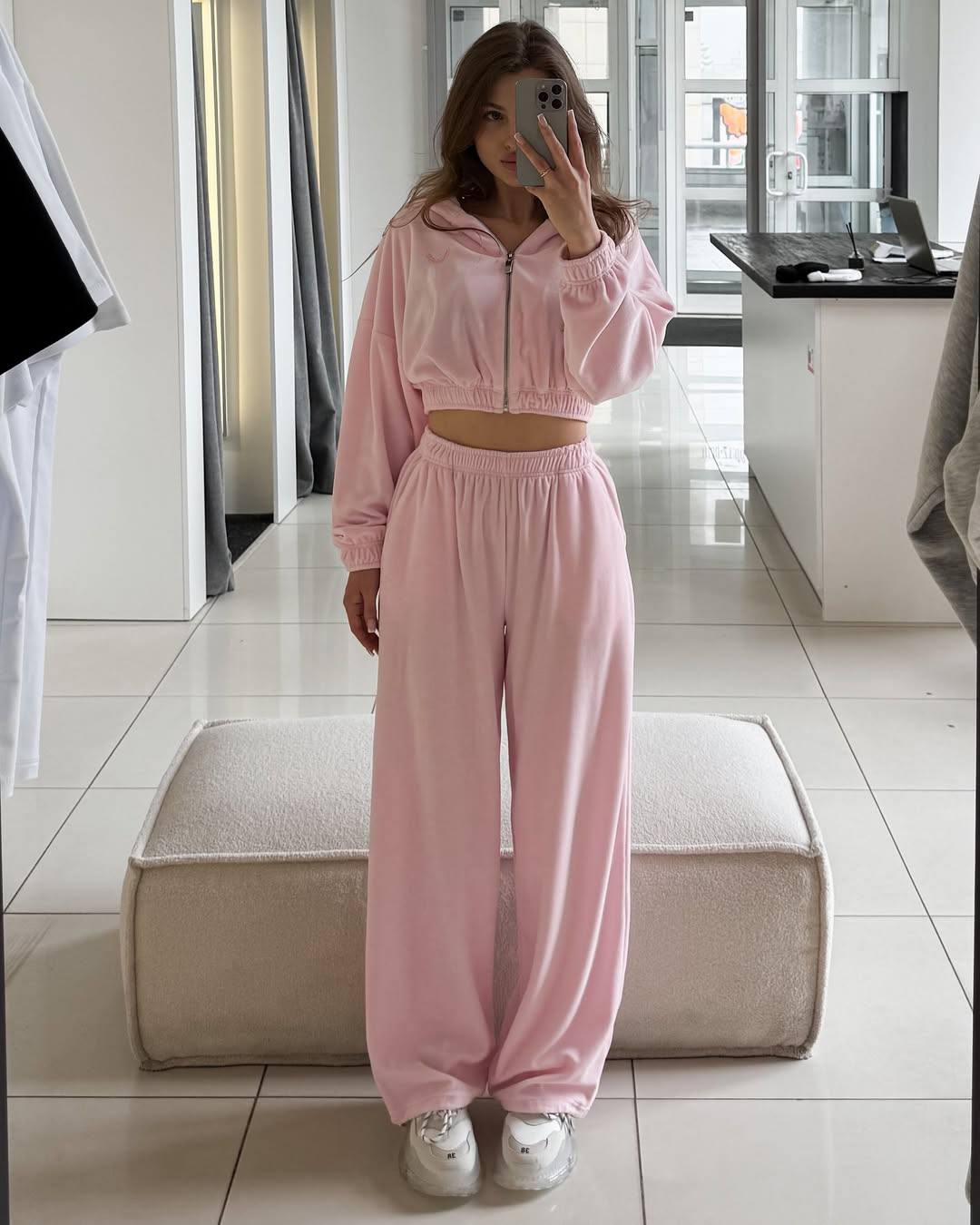 Person wearing a pink tracksuit taking a mirror selfie in a room.