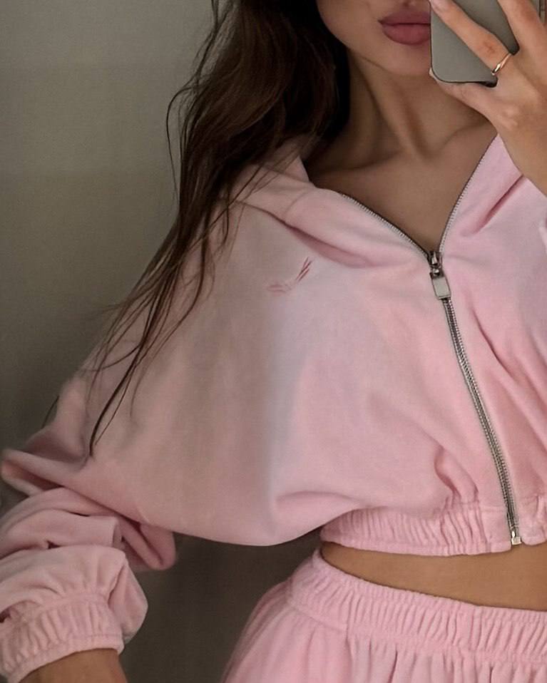 Person wearing a pink tracksuit taking a mirror selfie.