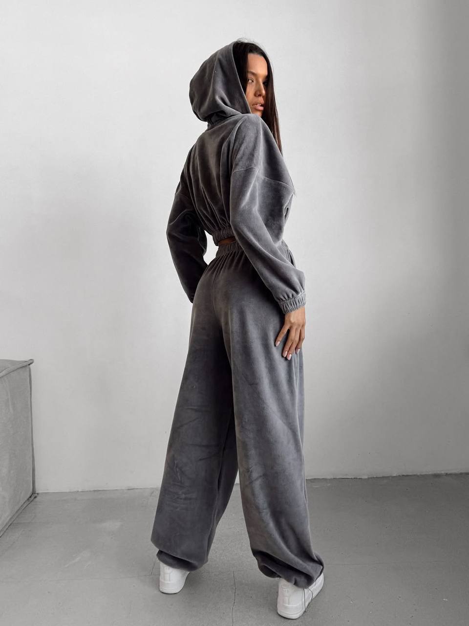 Person wearing a gray hoodie and wide-leg pants against a plain background