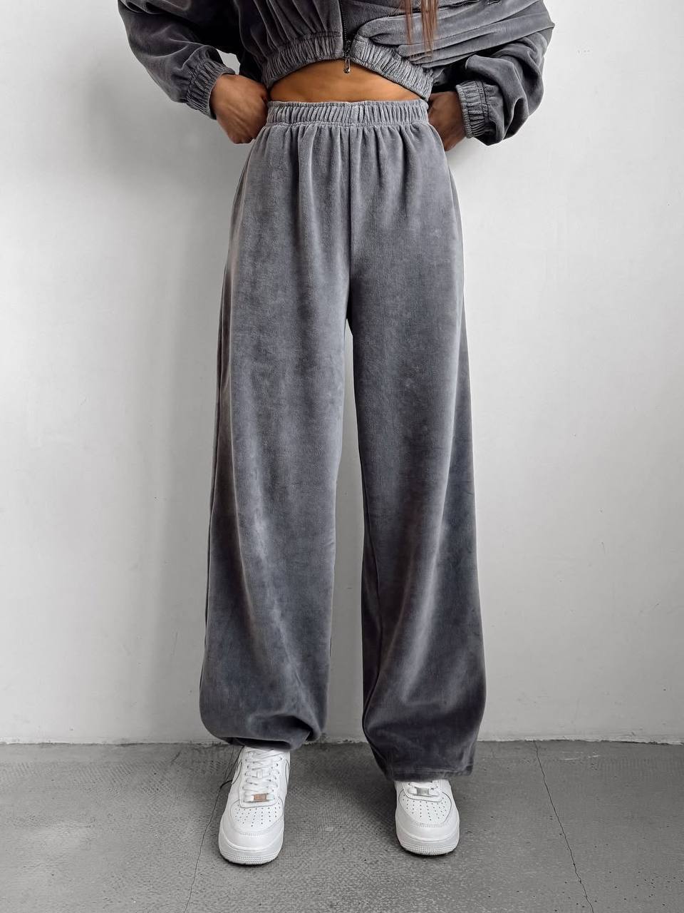 Person wearing gray velour pants and white sneakers against a plain background