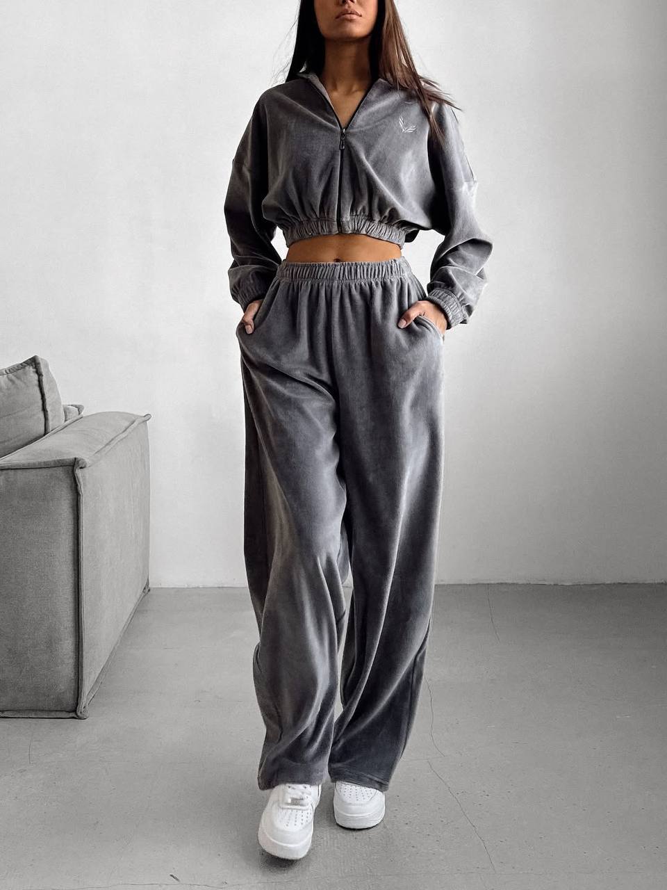 Person wearing a gray tracksuit in a minimalistic room with a gray sofa.