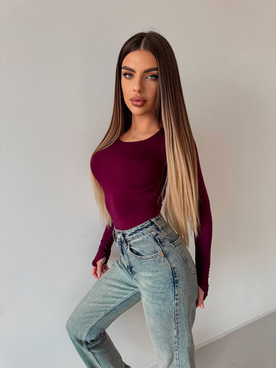 Woman wearing a burgundy top and light blue jeans against a plain background