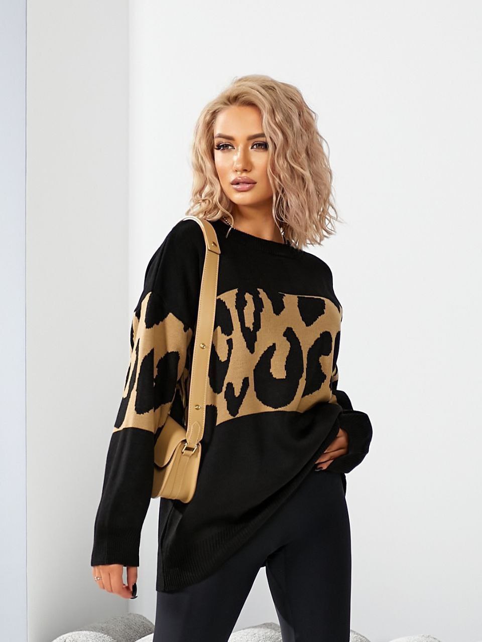 Woman wearing a black sweater with a leopard print pattern and a beige bag.