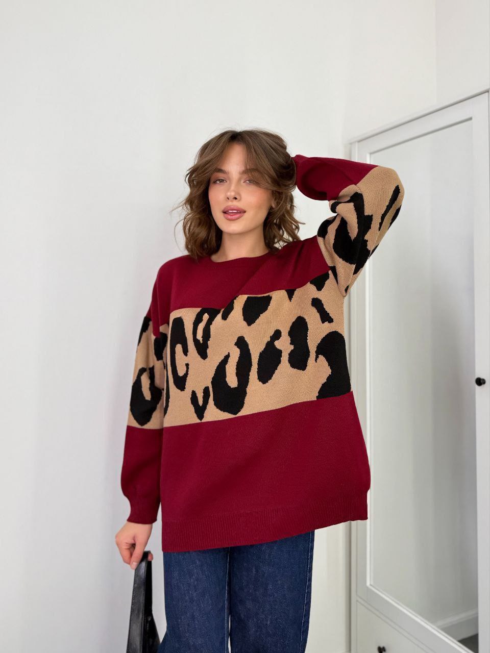 Woman wearing a maroon sweater with a leopard print pattern against a white wall.