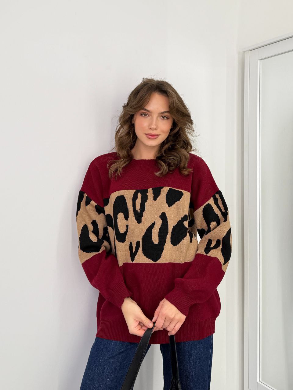 Woman wearing a maroon sweater with leopard print pattern against a white wall.