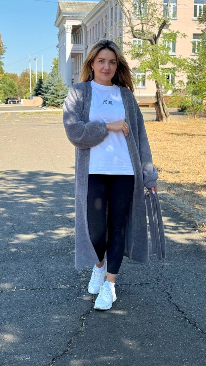 Woman wearing a long gray cardigan, white shirt, black leggings, and white sneakers on a street.
