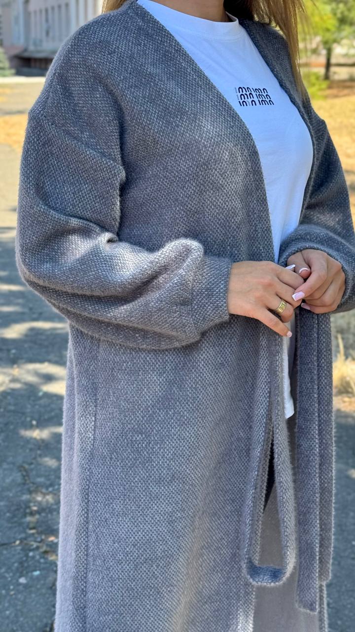 Person wearing a gray cardigan over a light blue shirt with text outdoors.