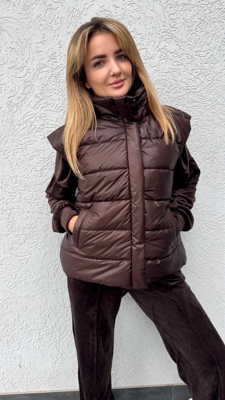 Woman wearing a brown puffer jacket against a textured white wall