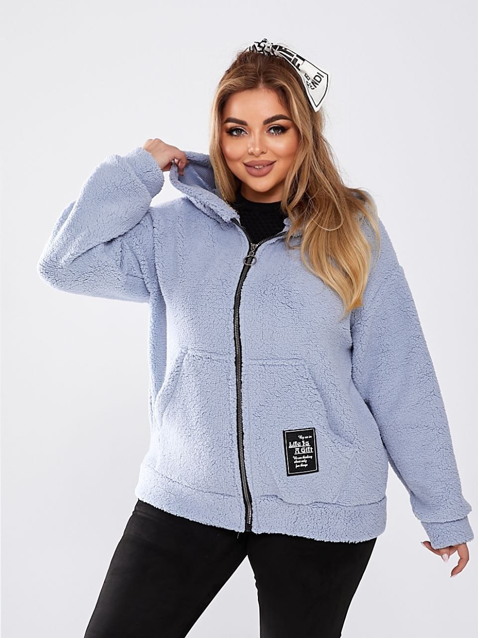 Woman wearing a light blue fleece jacket with a brand patch on a white background