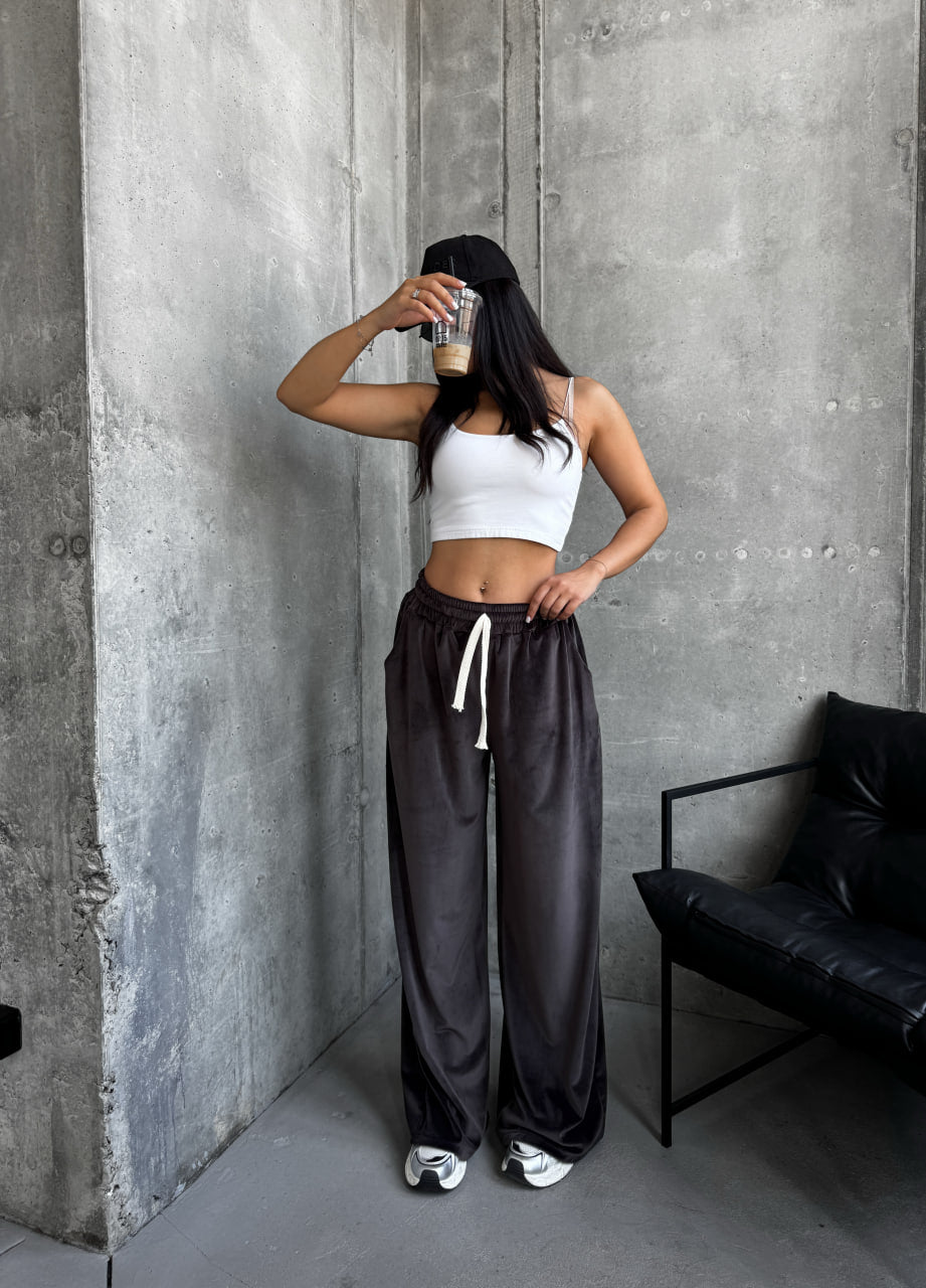 Person wearing a white crop top and dark pants against a concrete wall.